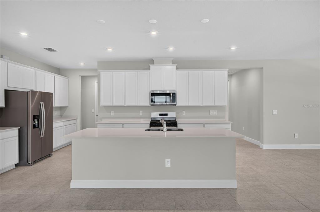 A kitchen features white shaker cabinets, stainless steel appliances, and a large quartz island — 9026 SUNDANCE TERRACE, PARRISH, FL