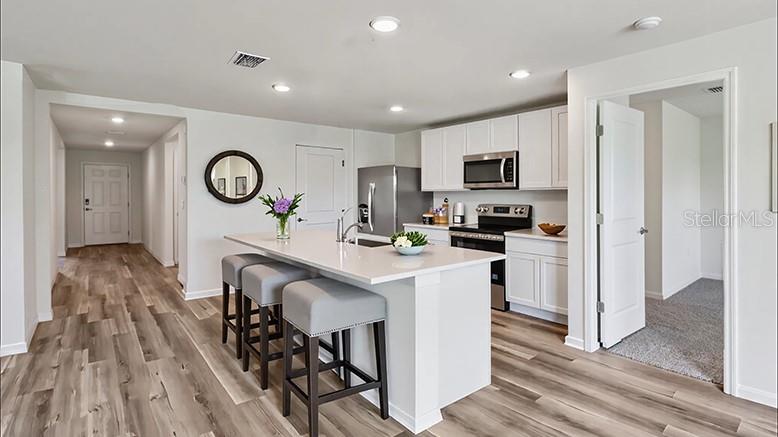A modern kitchen features white cabinetry, a quartz island with bar seating, and wood-look flooring — 8782 TRIUMPH CIRCLE, WILDWOOD, FL