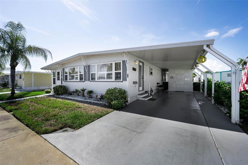 A white mobile home with a carport and a small front lawn under a blue sky — 143 MELODY LANE, TARPON SPRINGS, FL