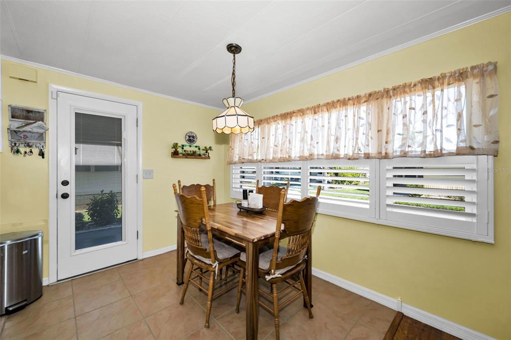 A dining area features a wooden table, four chairs, tile flooring, and a window with shutters — 143 MELODY LANE, TARPON SPRINGS, FL