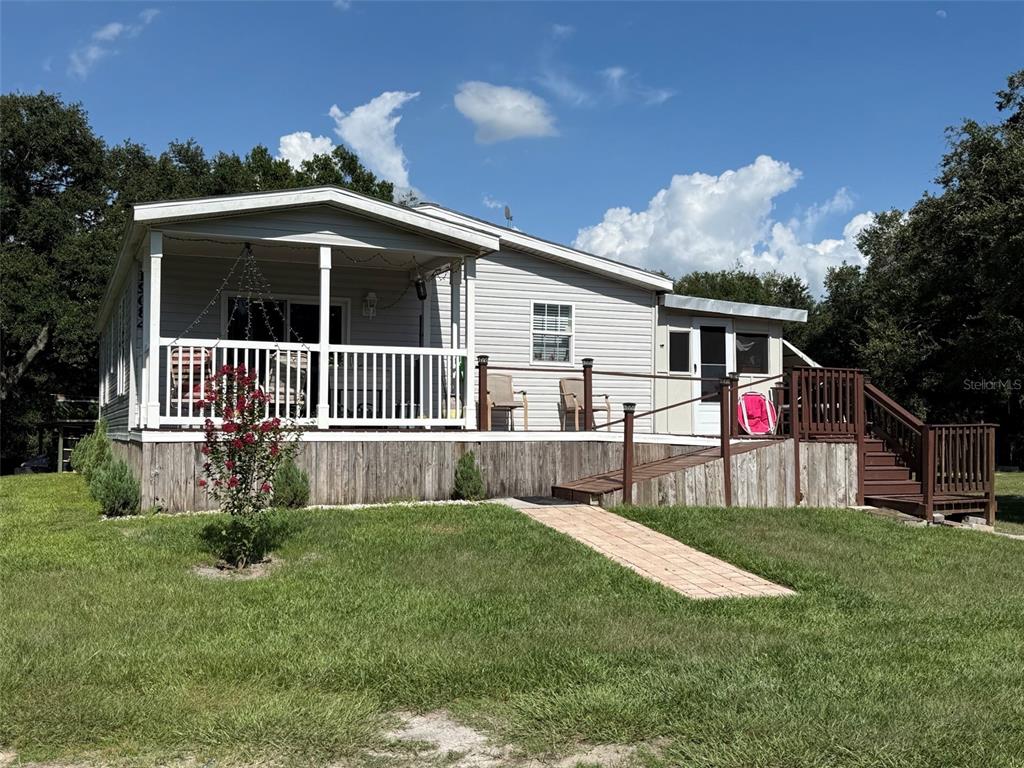 A light gray manufactured home features a large front porch, a ramp, and wooden stairs — 19084 NW 306TH STREET, OKEECHOBEE, FL