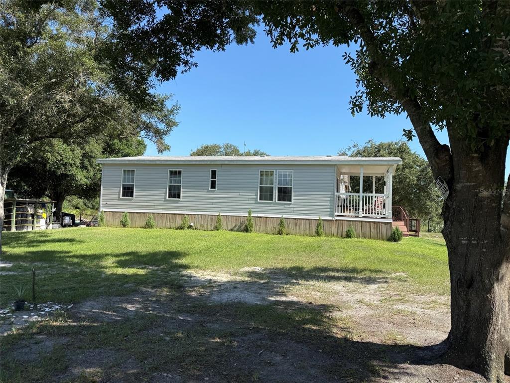 A light-colored manufactured home sits on a grassy lot with a wooden porch and skirting — 19084 NW 306TH STREET, OKEECHOBEE, FL
