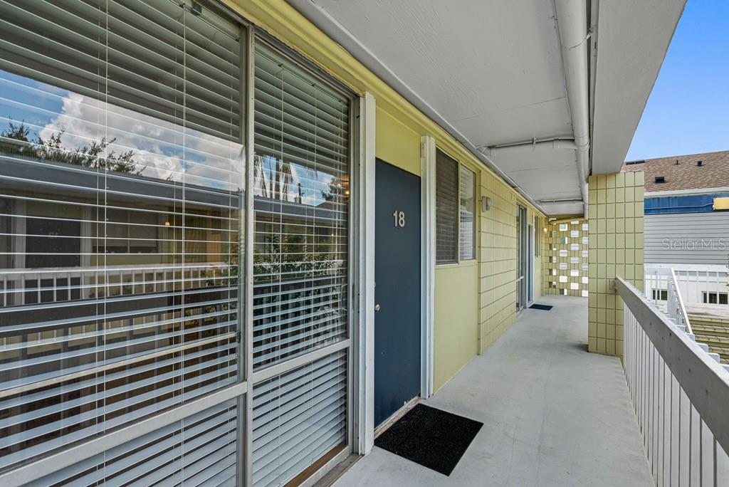 An exterior walkway leads to a dark blue apartment door numbered 18 with large windows — 1301 S HOWARD AVENUE UNIT C18, TAMPA, FL