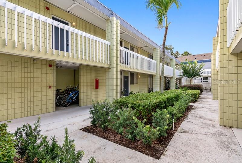 An exterior view of a two-story apartment building with a walkway and landscaped garden — 1301 S HOWARD AVENUE UNIT C18, TAMPA, FL