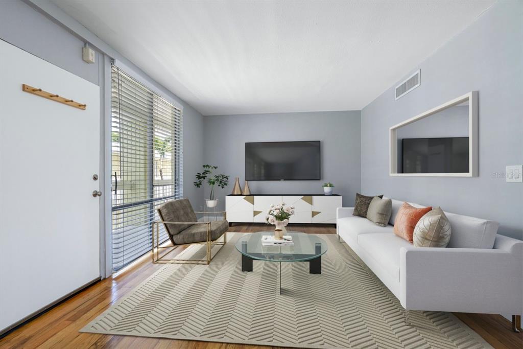 A living room with a white sofa, glass coffee table, TV console, and large window — 1301 S HOWARD AVENUE UNIT C18, TAMPA, FL