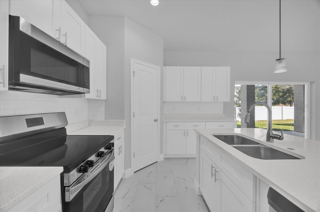 A modern kitchen features white cabinets, stainless steel appliances, a center island, and tile flooring — 1252 ASH TREE COVE, CASSELBERRY, FL