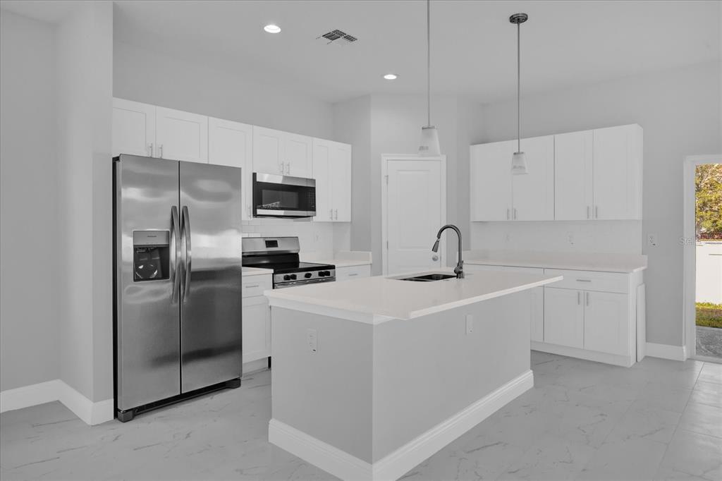 A modern kitchen features white cabinetry, stainless steel appliances, a center island, and light flooring — 1252 ASH TREE COVE, CASSELBERRY, FL
