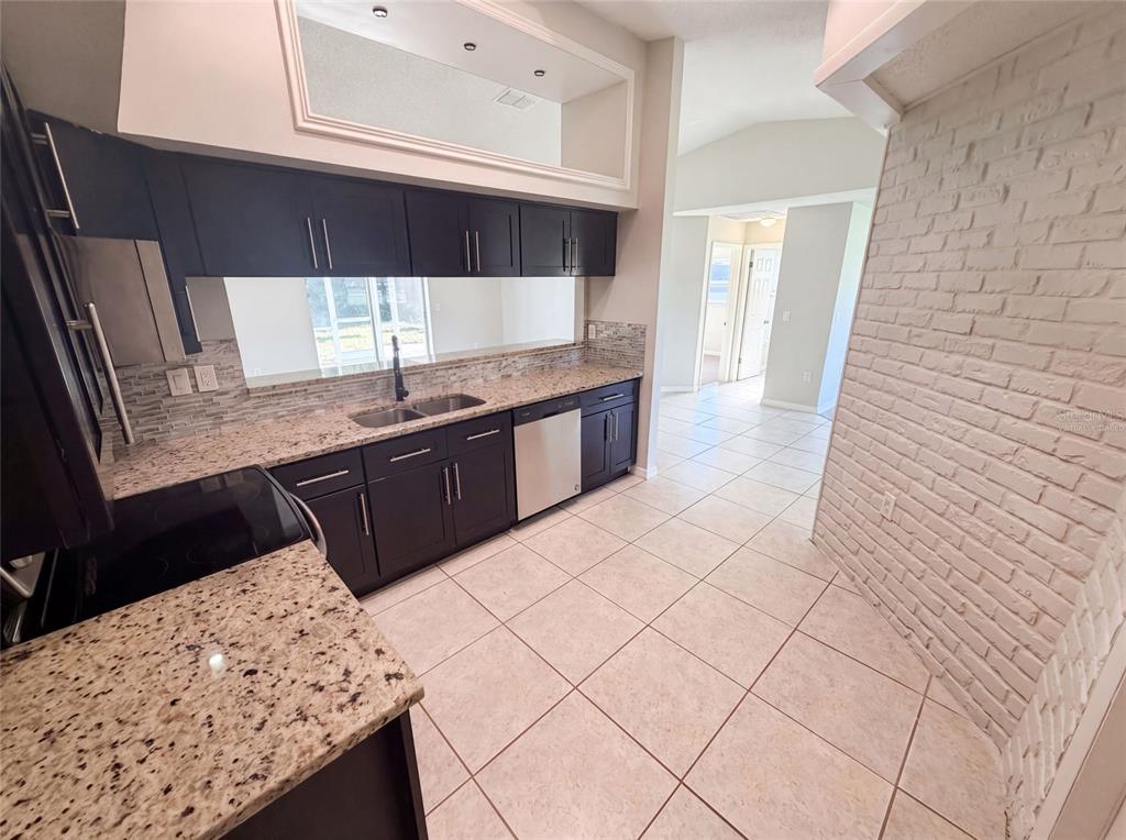 A kitchen features dark cabinets, granite countertops, a tiled backsplash, and a white brick wall — 11339 STACY STREET, SPRING HILL, FL