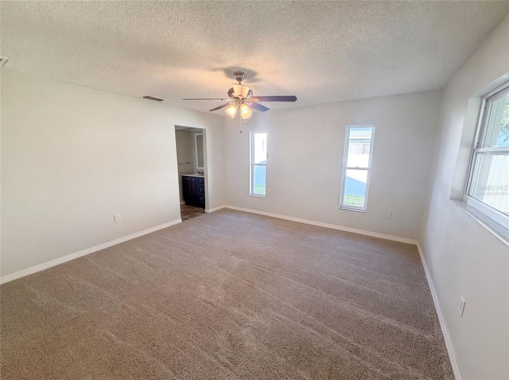 A carpeted bedroom features a ceiling fan, two windows, and a doorway to a bathroom — 11339 STACY STREET, SPRING HILL, FL