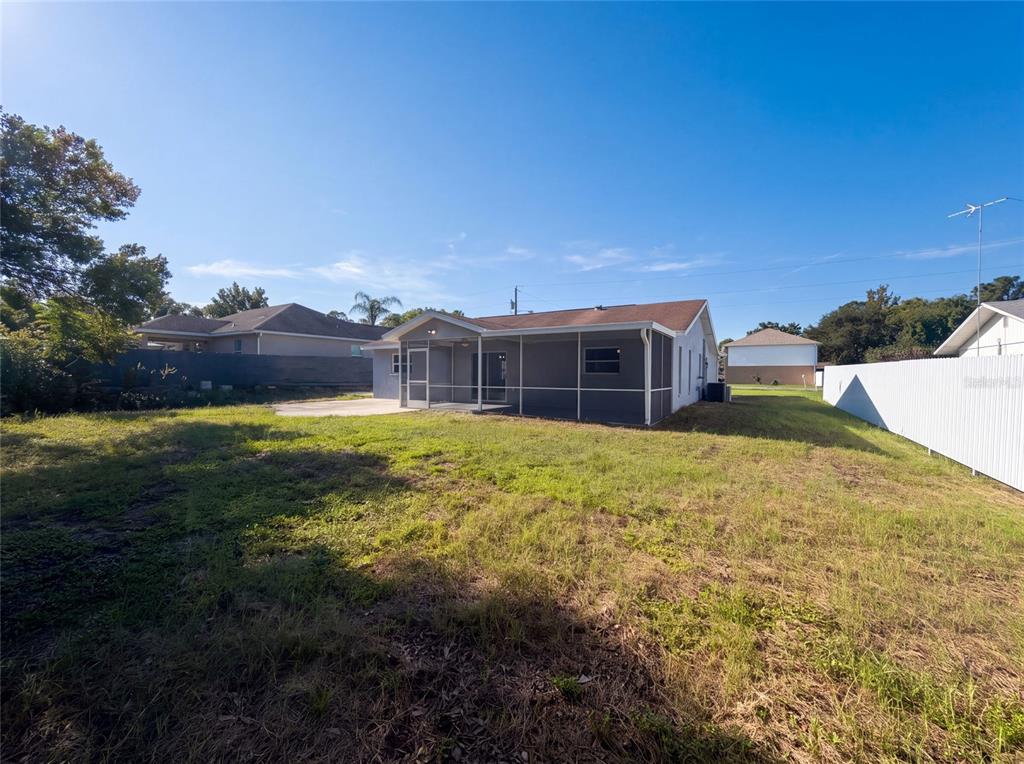 A gray house with a screened-in back porch sits on a large, grassy lot — 11339 STACY STREET, SPRING HILL, FL