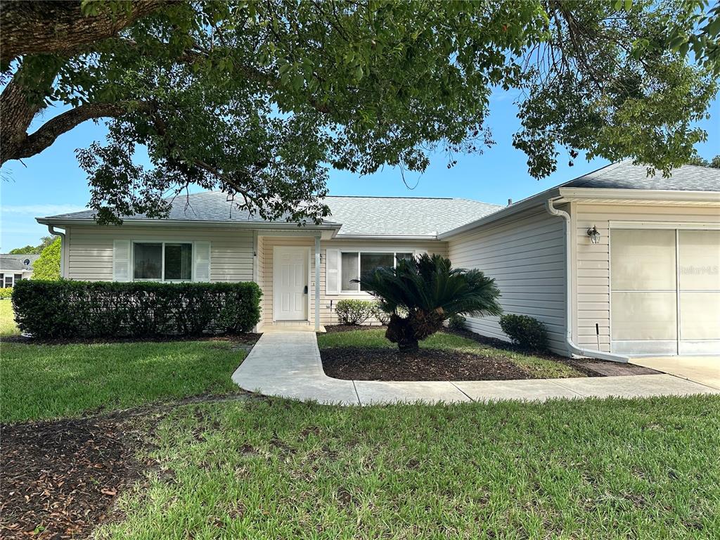 A single-story house with light siding, a concrete walkway, and a large tree in front — 13780 SW 115TH CIRCLE, DUNNELLON, FL