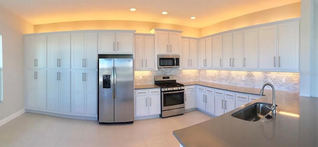 A modern kitchen features white cabinetry, stainless steel appliances, and gray countertops — 30791 LINDENTREE DRIVE, WESLEY CHAPEL, FL
