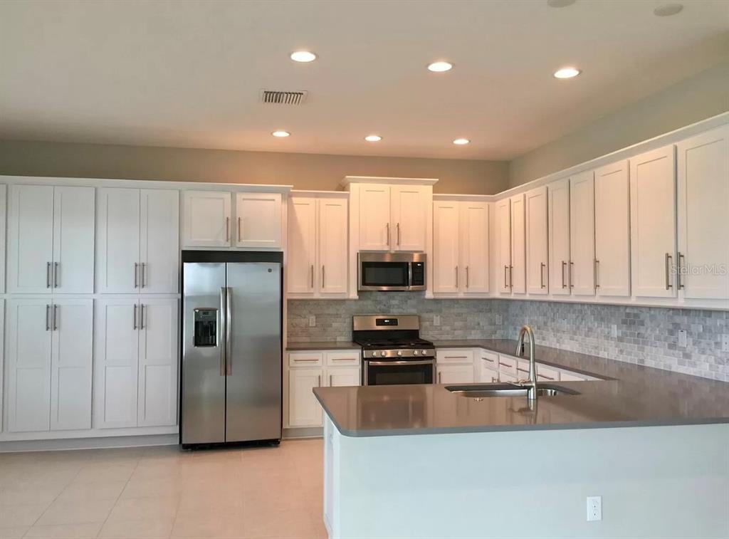 A kitchen with white cabinets, stainless steel appliances, gray countertops, and a tile backsplash — 30791 LINDENTREE DRIVE, WESLEY CHAPEL, FL