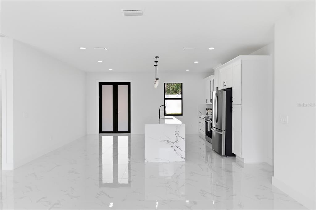 A modern kitchen features white cabinetry, a marble-topped island, and glossy white tile flooring — 27426 AZEN LOOP, BROOKSVILLE, FL