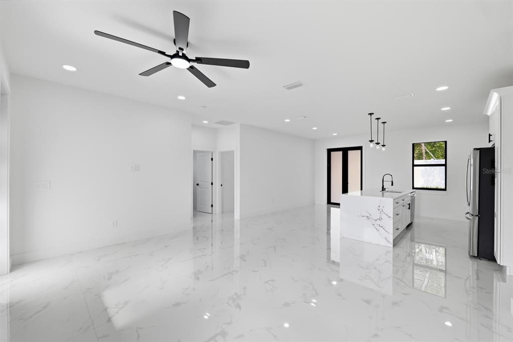 A bright, open-concept kitchen and living area features white marble-look tile flooring and a ceiling fan — 27426 AZEN LOOP, BROOKSVILLE, FL