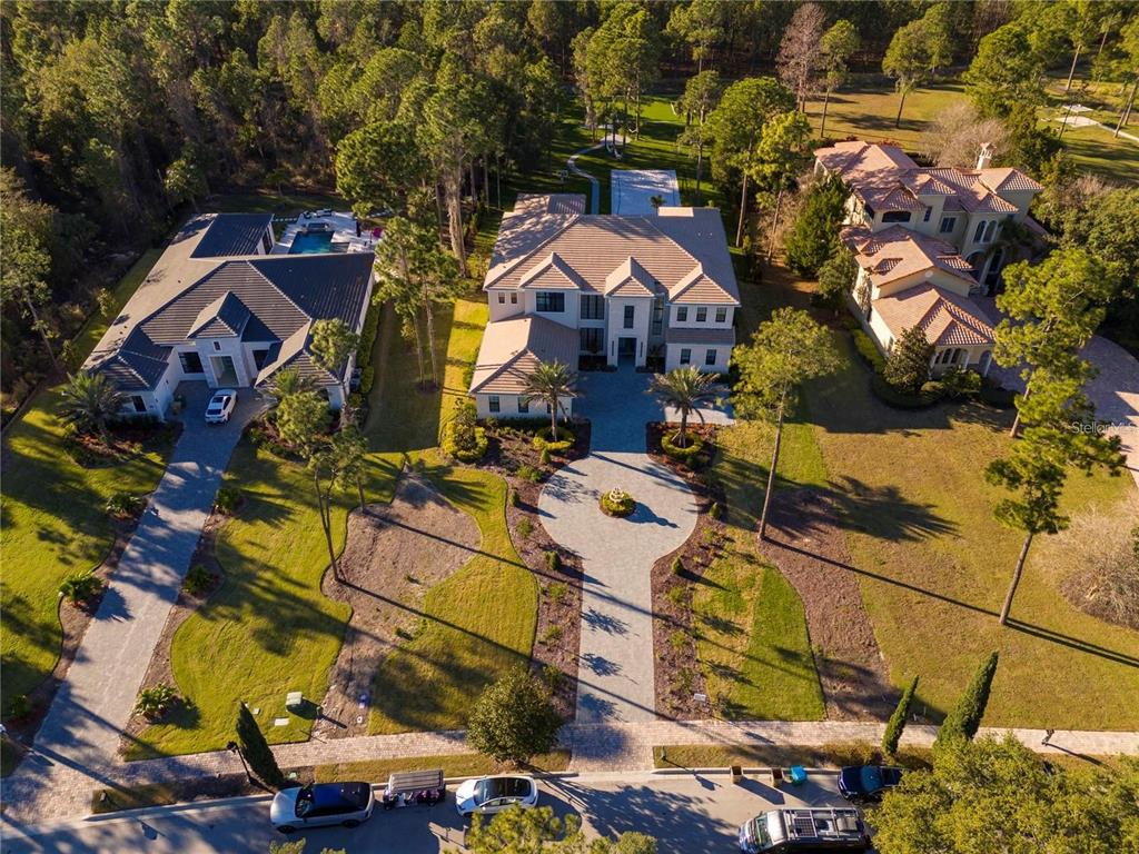An aerial view shows three large houses with paved driveways and pools surrounded by wooded grounds — 15926 PENDIO DRIVE, BELLA COLLINA, FL