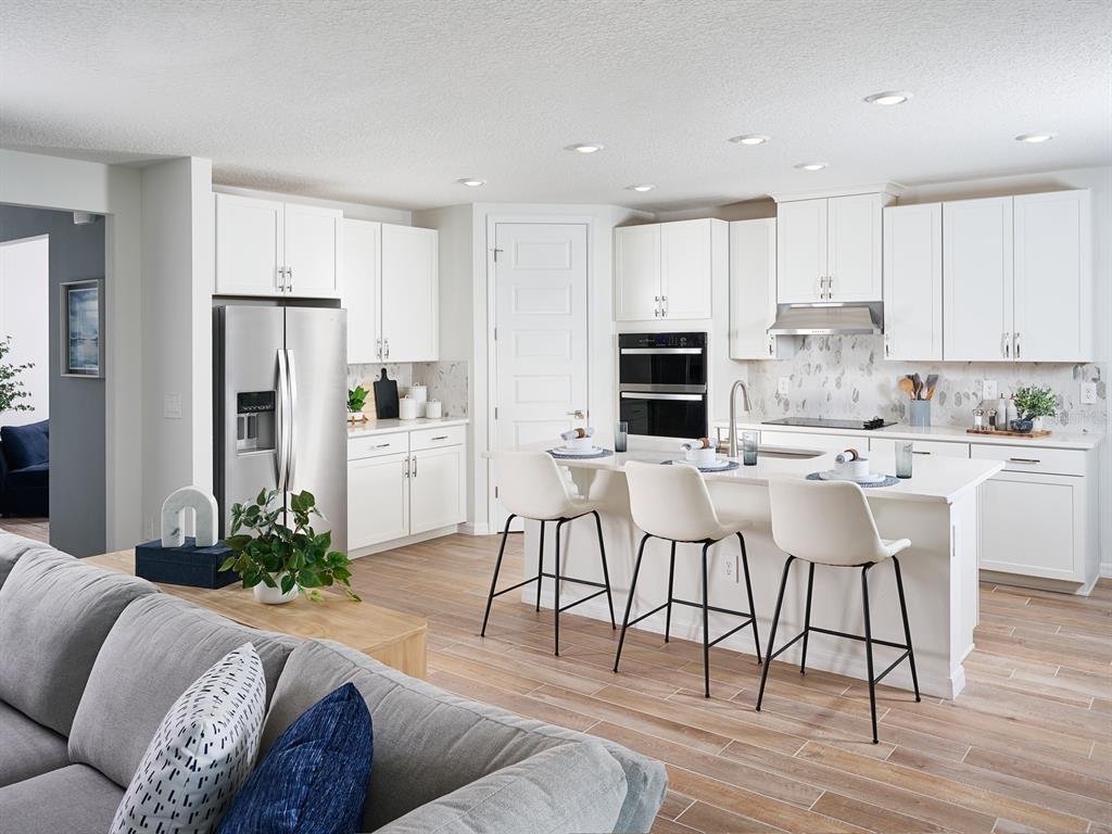 A modern kitchen with white cabinets, stainless steel appliances, and a central island with seating — 14152 HARVEST PINES LANE, HUDSON, FL