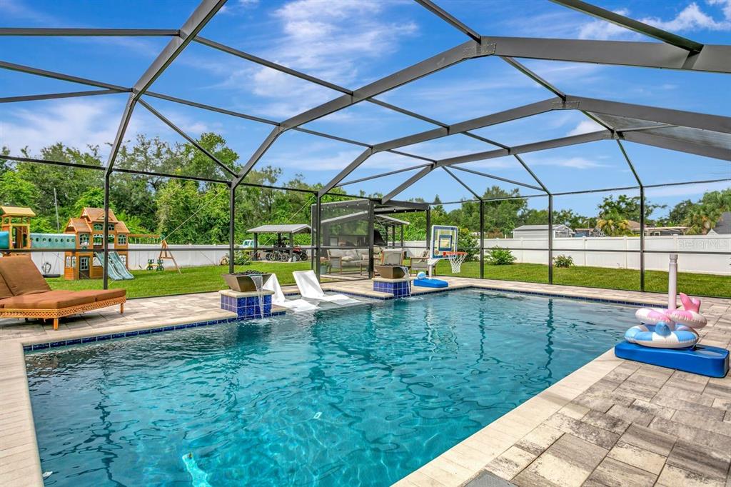 A screened-in swimming pool with a water feature, lounge chairs, and a backyard playground — 12007 VERMILLION WAY, RIVERVIEW, FL
