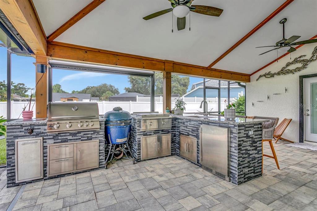 An outdoor kitchen features stainless steel appliances, a blue ceramic grill, and stone veneer cabinetry — 12007 VERMILLION WAY, RIVERVIEW, FL
