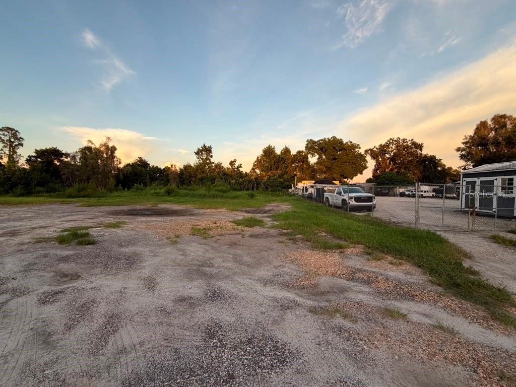 An expansive, flat dirt lot bordered by a chain-link fence and mature trees at sunset — 6012 LAND O LAKES BOULEVARD, LAND O LAKES, FL