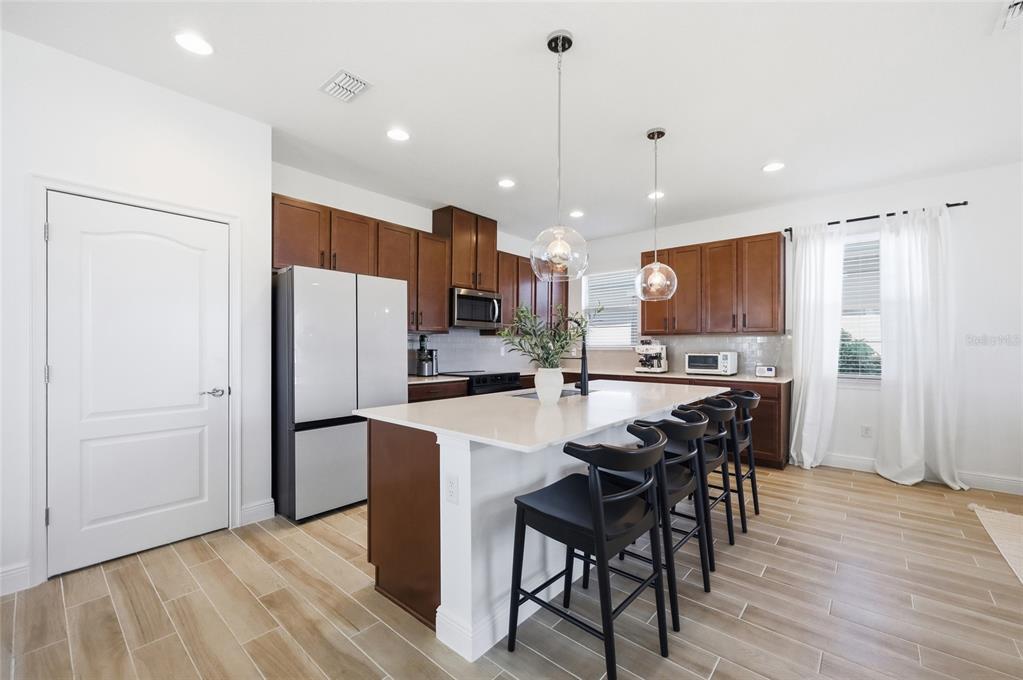 A kitchen features dark wood cabinets, a white island with black stools, and light flooring — 6699 ALDER ROAD, ST CLOUD, FL