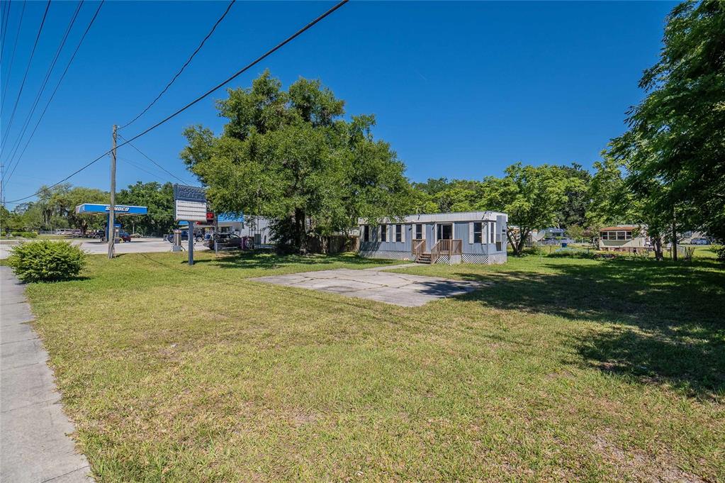 A small, light-colored mobile home sits on a grassy lot next to a gas station — 632 COMMONWEALTH AVENUE SW, POLK CITY, FL