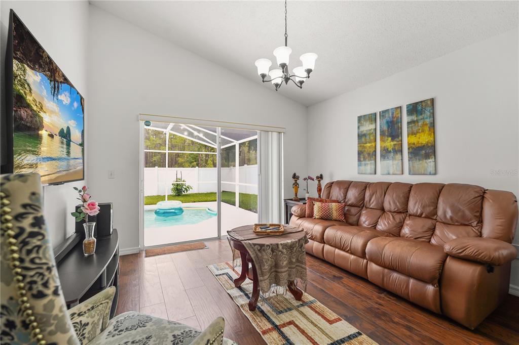 A living room with a brown leather sofa, wood floors, and a view of a pool — 638 PINE CONE DRIVE, DAVENPORT, FL