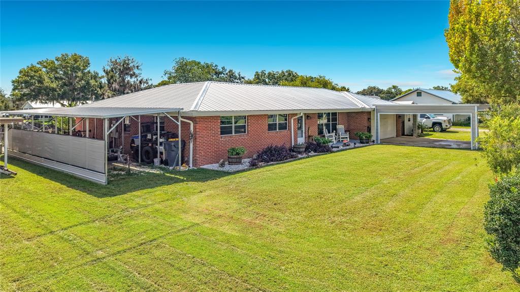 A single-story brick house features a metal roof, a side carport, and a large lawn — 116 BREAM STREET, HAINES CITY, FL