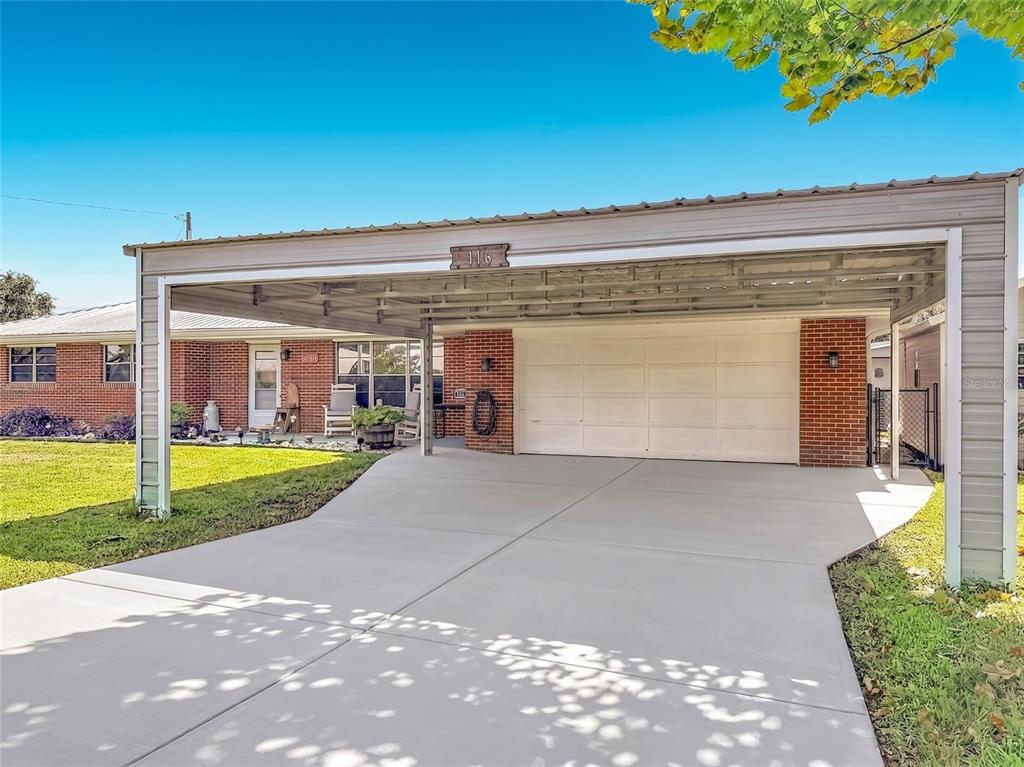 A brick house features a large metal carport covering a concrete driveway and garage door — 116 BREAM STREET, HAINES CITY, FL