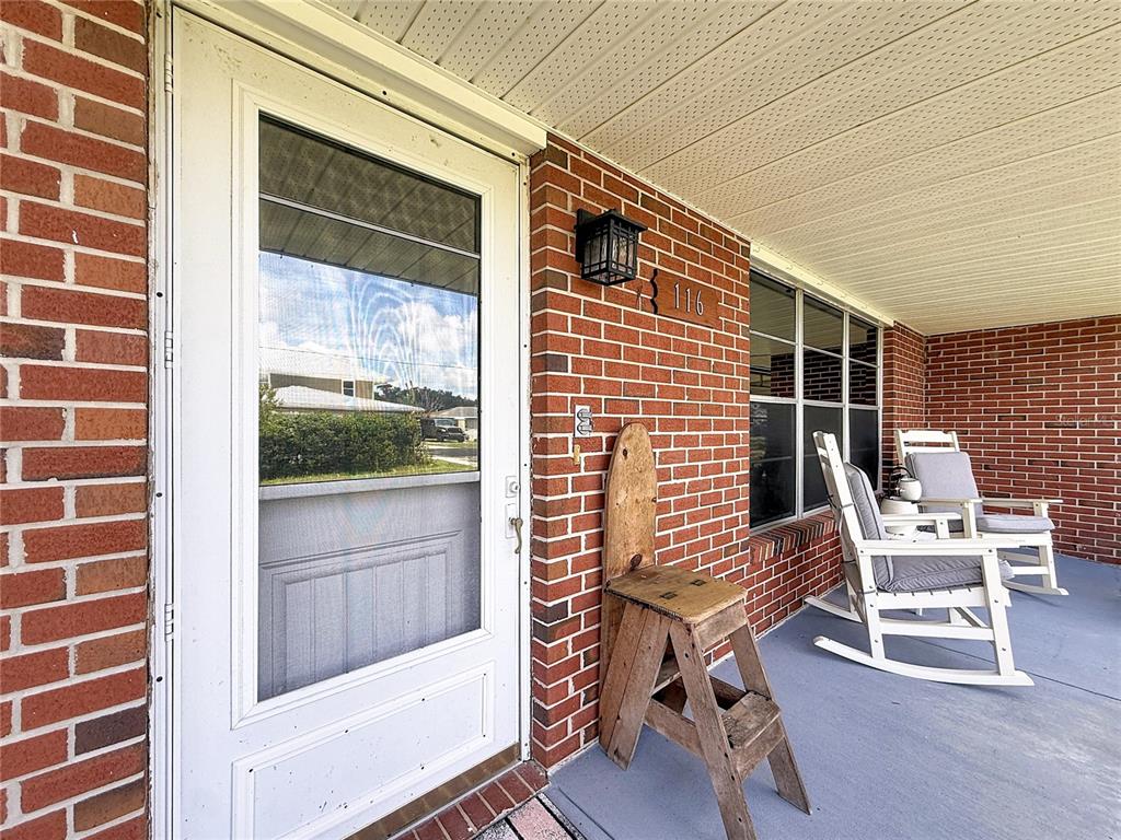 A brick porch features a white storm door, a wooden step stool, and two rocking chairs — 116 BREAM STREET, HAINES CITY, FL