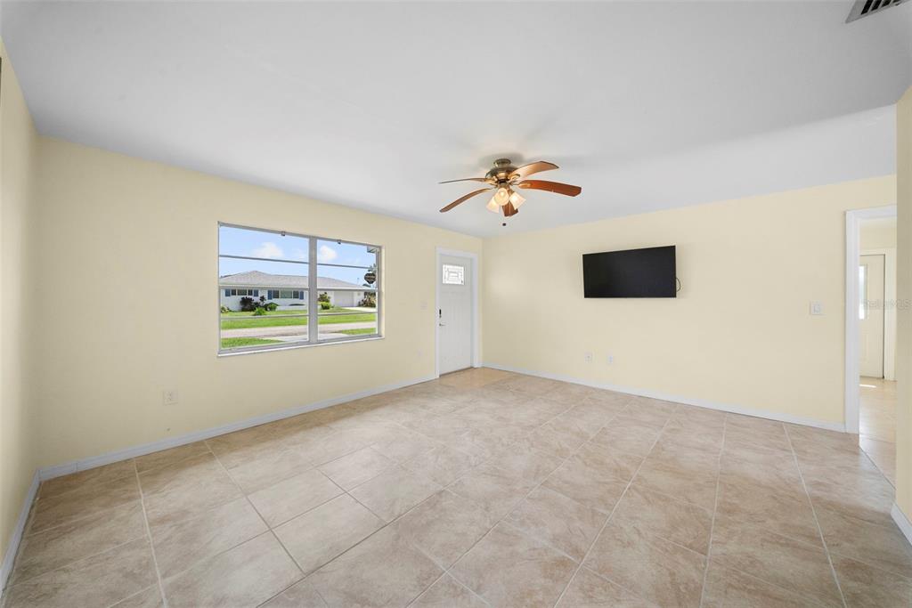 A living room with light yellow walls, tile flooring, a ceiling fan, and a wall-mounted television — 154 DANFORTH DRIVE, PUNTA GORDA, FL