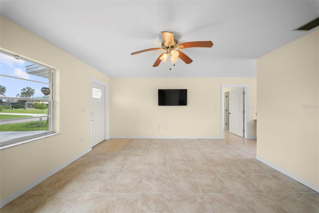 A living room features light yellow walls, tile flooring, a ceiling fan, and a wall-mounted television — 154 DANFORTH DRIVE, PUNTA GORDA, FL