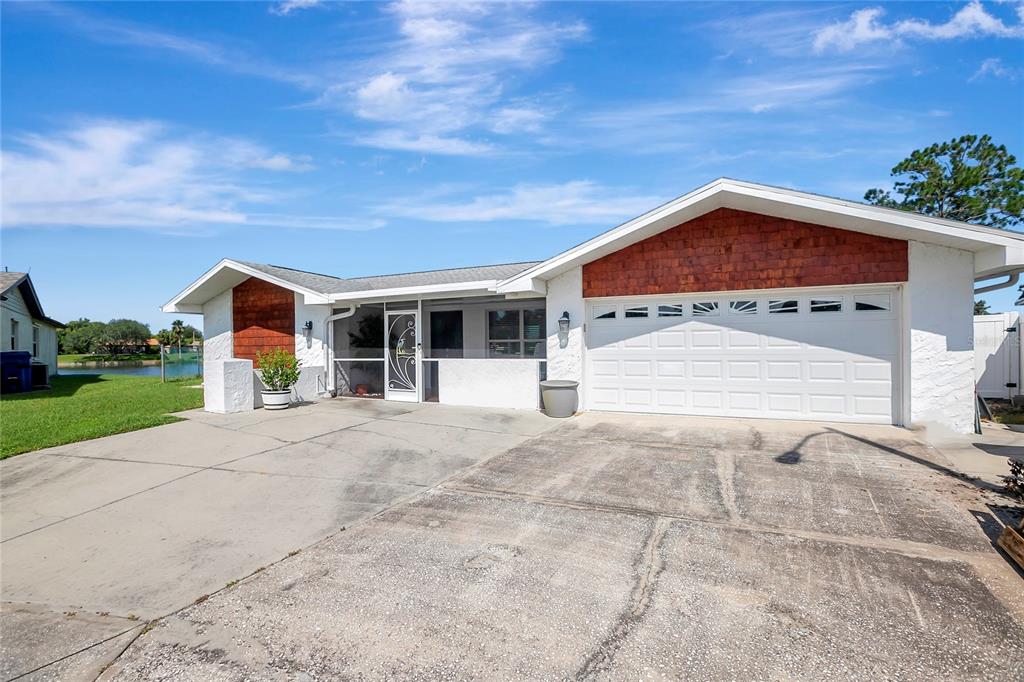 A single-story house with a white stucco exterior, wood-shingle accents, and a two-car garage — 9619 TOWANDA LANE, PORT RICHEY, FL