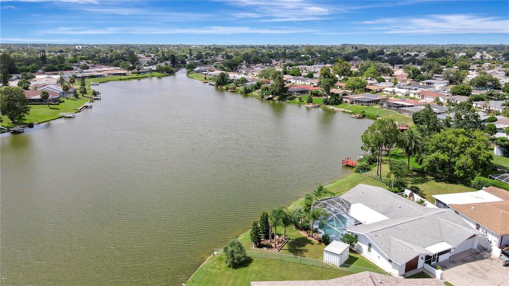 An aerial view shows a waterfront house with a screened pool deck beside a lake — 9619 TOWANDA LANE, PORT RICHEY, FL