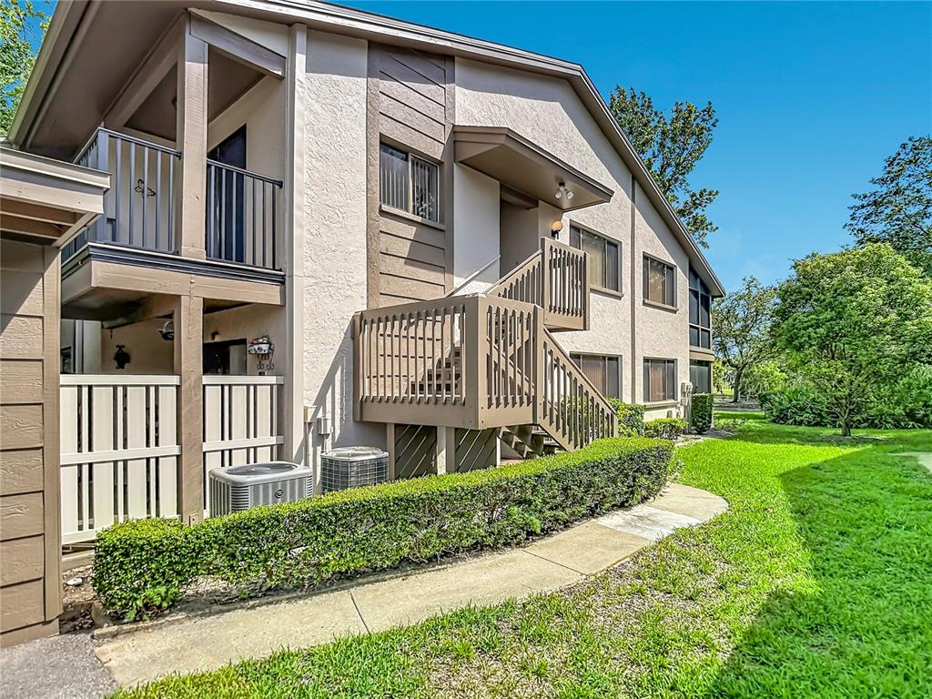 A two-story apartment building exterior features a wooden staircase, balcony, and a manicured hedge — 12913 FAIRWAY DRIVE UNIT D, HUDSON, FL
