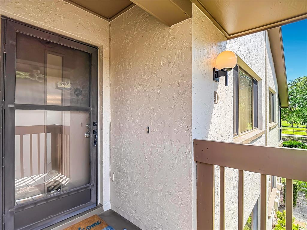 A brown storm door leads to a covered entryway with a wall-mounted light fixture — 12913 FAIRWAY DRIVE UNIT D, HUDSON, FL