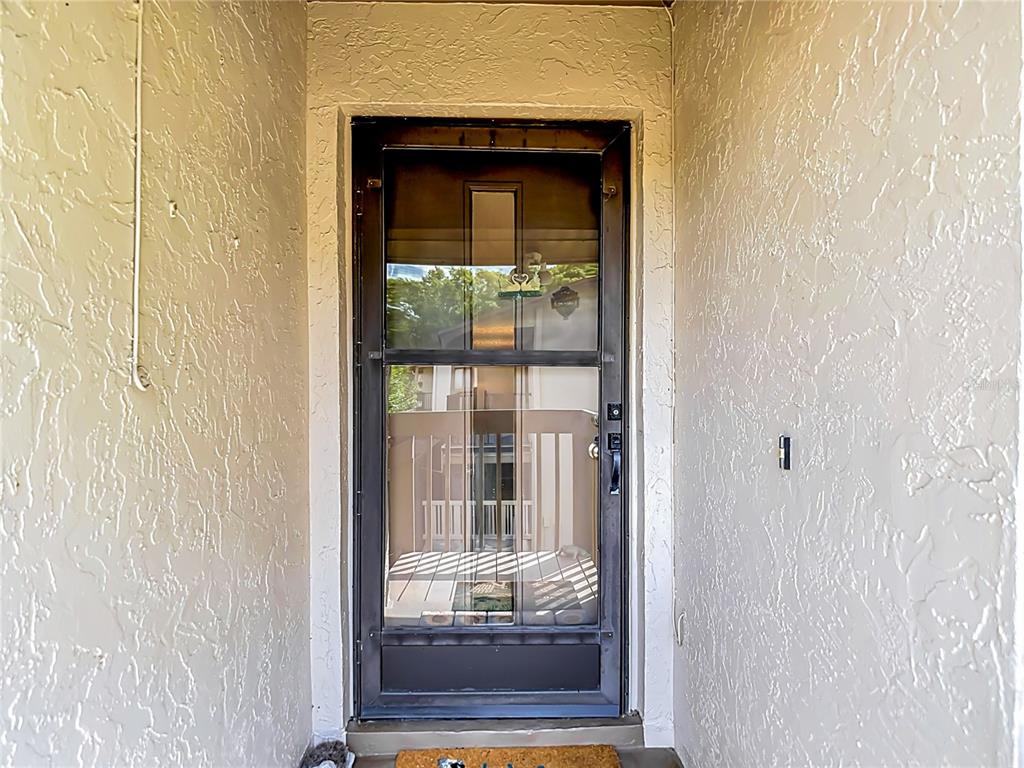 A dark-framed storm door is centered between textured, light-colored walls in an entryway — 12913 FAIRWAY DRIVE UNIT D, HUDSON, FL