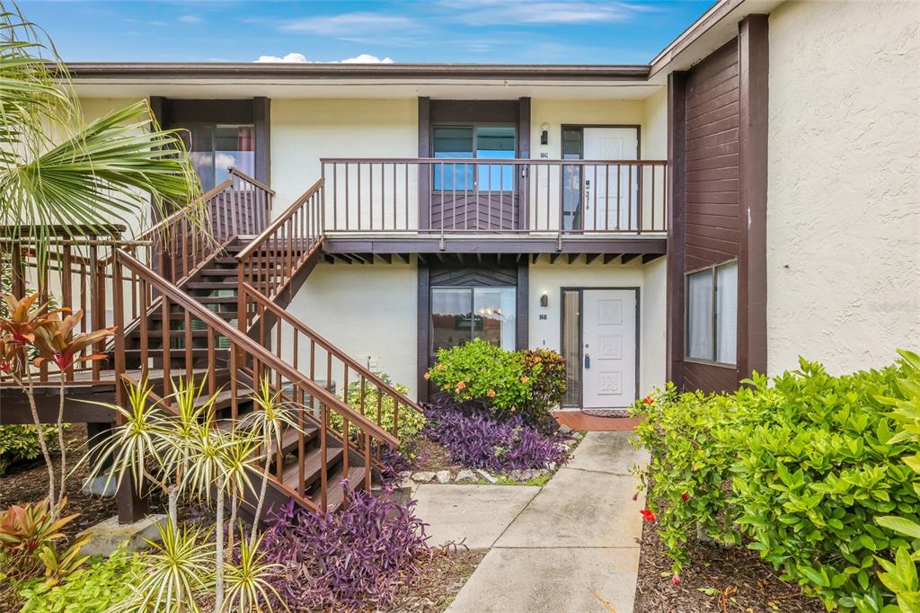 An exterior view of a two-story apartment building with wooden stairs and a concrete walkway — 5400 34TH STREET W UNIT B16, BRADENTON, FL