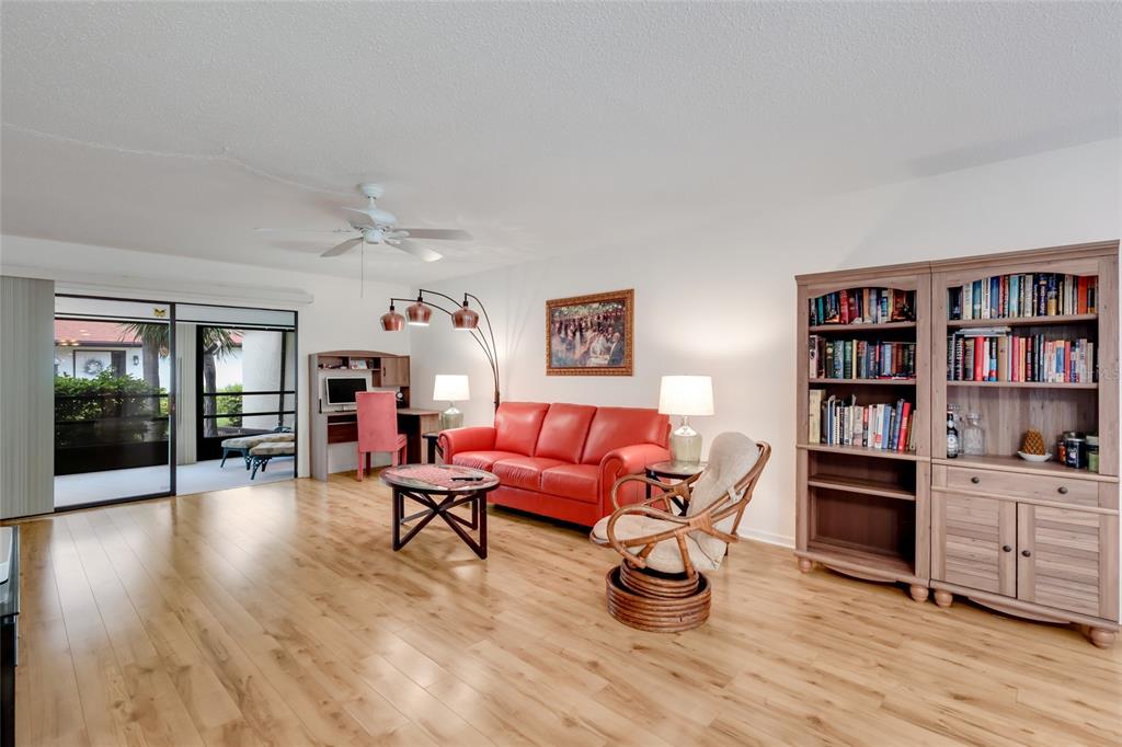 A living room features light wood flooring, a red sofa, a bookshelf, and a sliding door — 5400 34TH STREET W UNIT B16, BRADENTON, FL