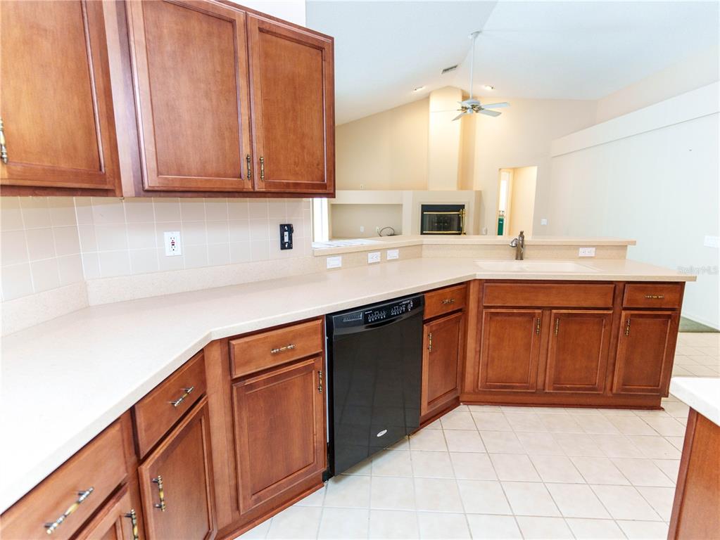 A kitchen features wood cabinets, light countertops, a black dishwasher, and tile flooring — 7709 TIMBERWYCK COURT, NEW PORT RICHEY, FL