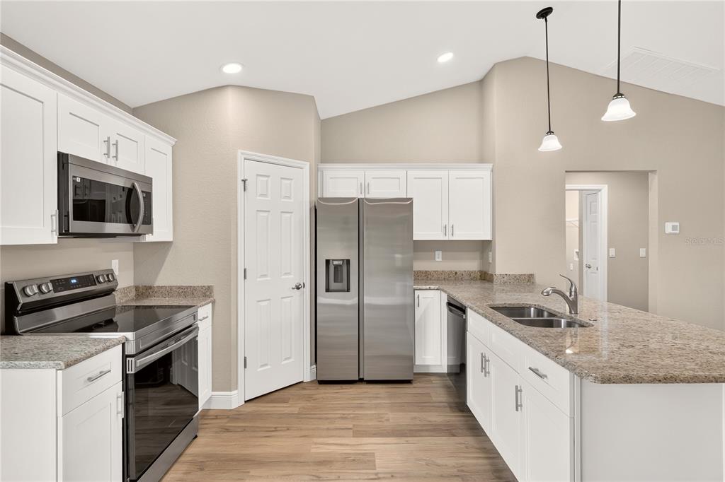 A kitchen with white cabinets, stainless steel appliances, and granite countertops under a vaulted ceiling — 19802 SW MARINE BOULEVARD, DUNNELLON, FL