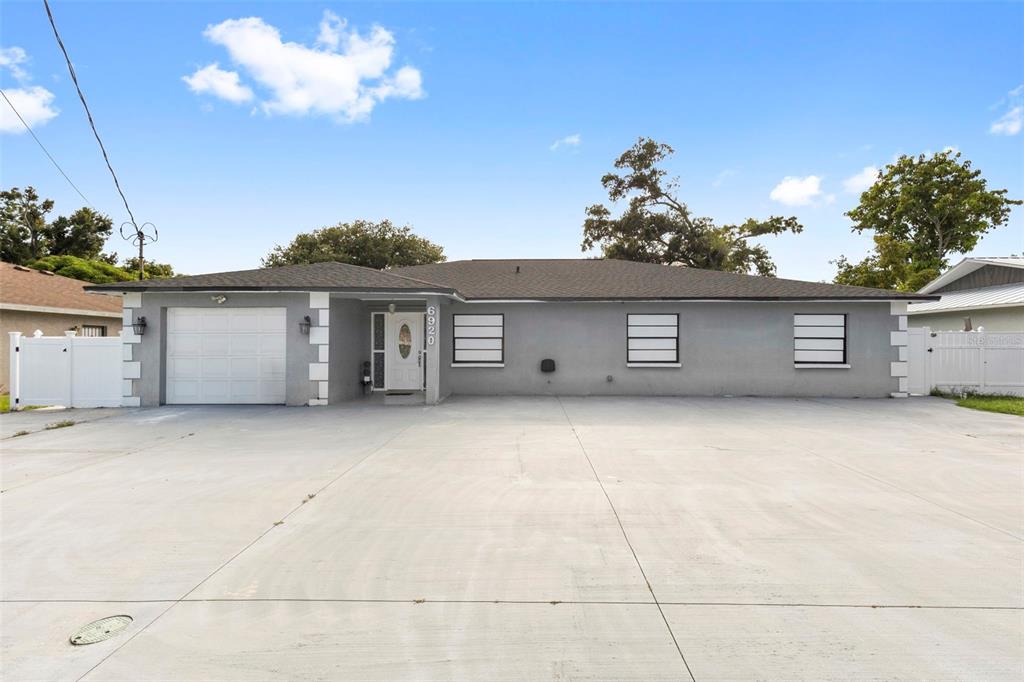 A single-story gray house with a white garage door and a large concrete driveway — 6920 N CAMERON AVENUE, TAMPA, FL