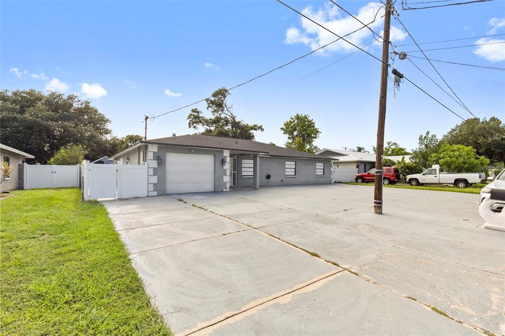 A gray single-story house features a white garage door, a concrete driveway, and a white fence — 6920 N CAMERON AVENUE, TAMPA, FL