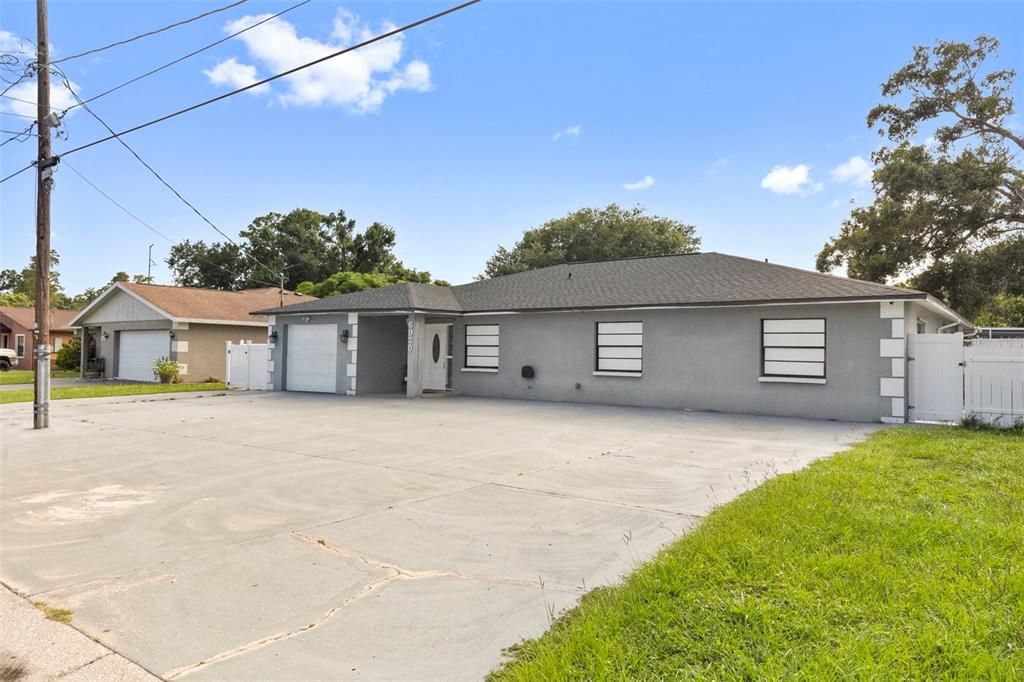 A single-story gray house with a large concrete driveway and a white garage door — 6920 N CAMERON AVENUE, TAMPA, FL