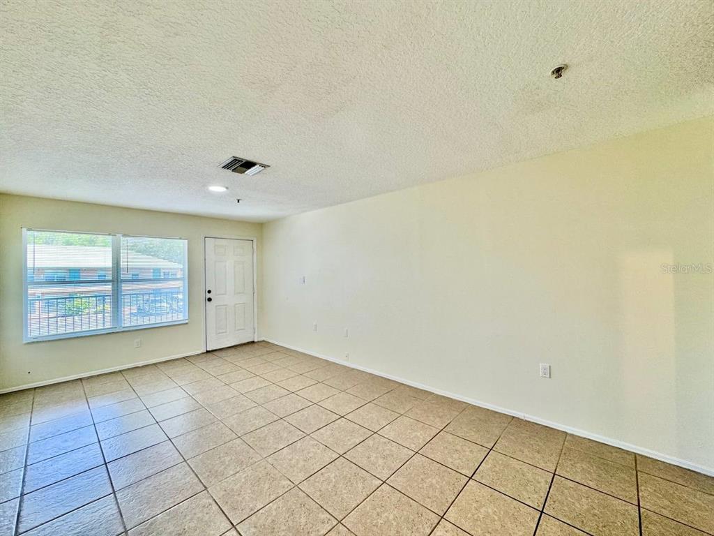 An empty room features beige tile flooring, a white door, and a large window — 5816 CONGRESS STREET UNIT 203, NEW PORT RICHEY, FL