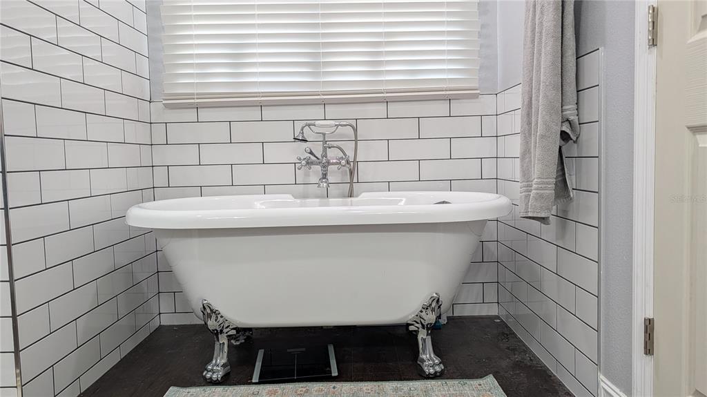 A white clawfoot bathtub sits against a wall with white subway tile and dark flooring — 345 CANNON STREET, LAKELAND, FL