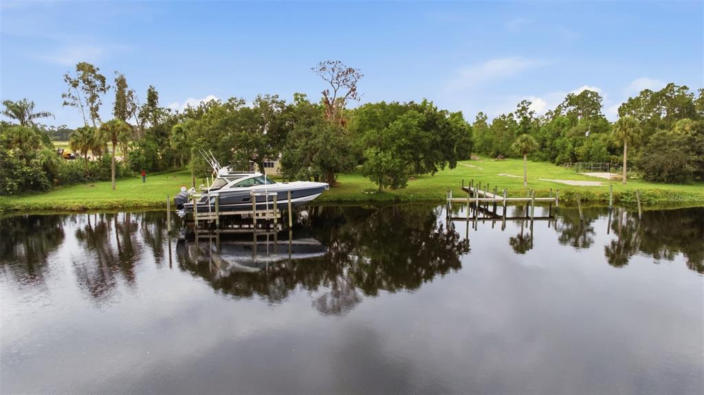 A boat is docked on a canal next to a grassy yard with trees — 13664 & 13668 MARQUETTE BOULEVARD, FORT MYERS, FL