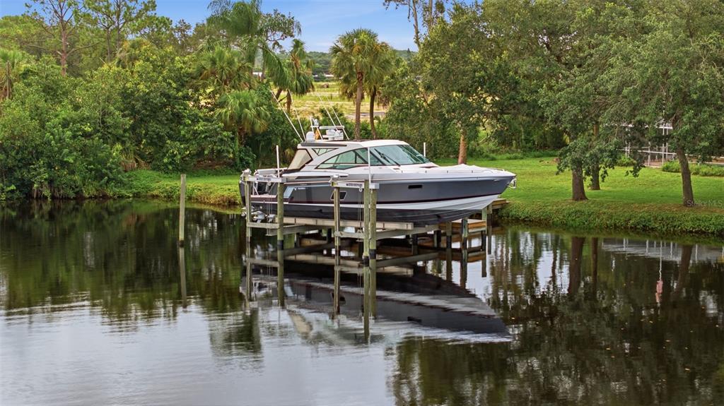 A motorboat is docked on a mechanical lift in a canal surrounded by lush greenery — 13664 & 13668 MARQUETTE BOULEVARD, FORT MYERS, FL