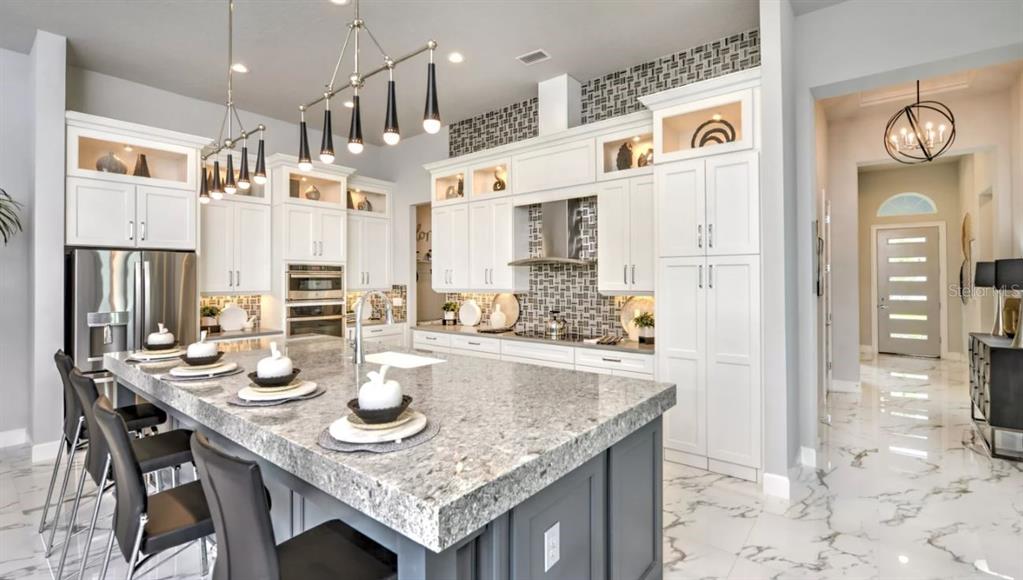 A modern kitchen features white cabinetry, a large granite island, and marble-style tile flooring — 441 STIRLING BRIDGE DRIVE, ORMOND BEACH, FL