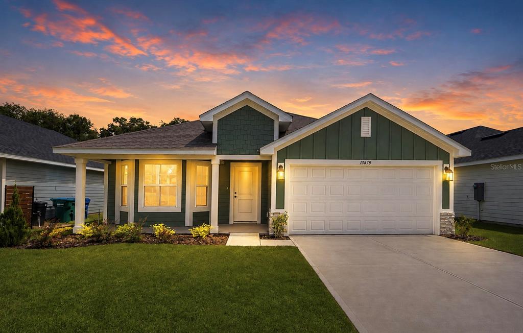 A single-story house with green siding, a white garage door, and a concrete driveway at sunset — 13879 NW 150TH CIRCLE, ALACHUA, FL